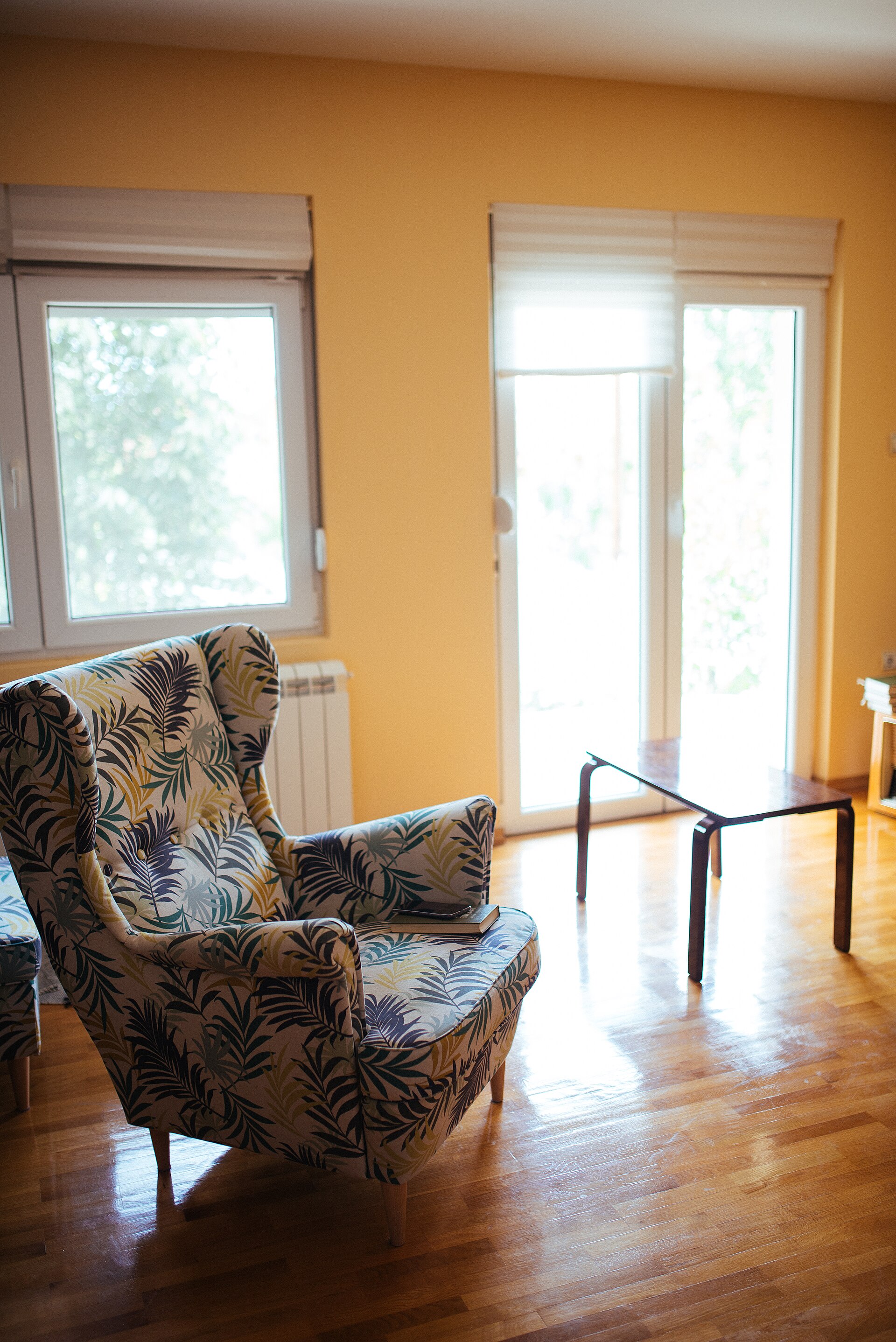 A cozy armchair with leaf-patterned fabric beside a bright window, in a warm and comfortable room